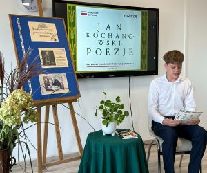 Uczeń klasy siódmej czyta poezję, siedząc na tle dekoracji okolicznościowej