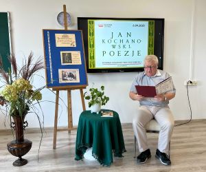 Nauczyciel historii czyta poezję, siedząc na tle dekoracji okolicznościowej