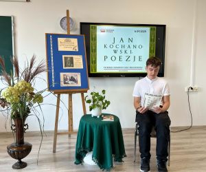 Uczeń klasy ósmej czyta poezję, siedząc na tle dekoracji okolicznościowej