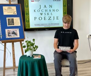 Uczeń klasy ósmej czyta poezję, siedząc na tle dekoracji okolicznościowej