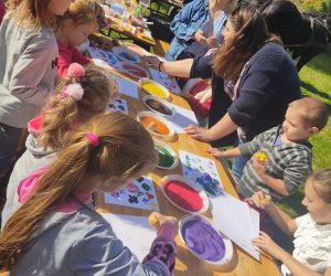 Dzieci siedzą przy stoliku na dworze i wykonują obrazki z pieczątek z ziemniaków.