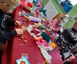 Dzieci siedzą przy stoliku wewnątrz budynku i wykonują obrazki z pieczątek z ziemniaków.