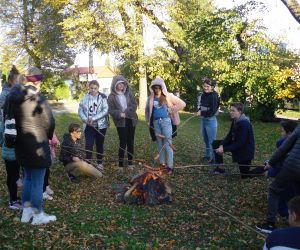 Dzieci znajdują się na świeżym powietrzu przy ognisku pieką kiełbaski. 