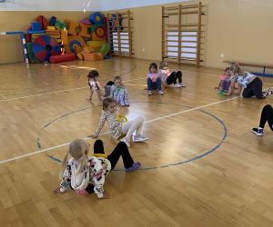 Młodsze dzieci uczestniczą w zabawie ruchowej w sali gimnastycznej, poruszając się w podporze tyłem.