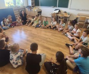 Uczniowie siedzą w kole i rozmawiają z prowadzącą zajęcia