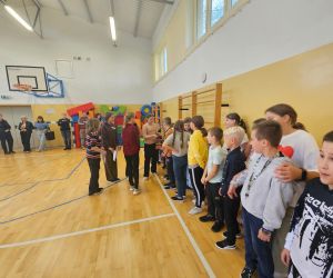 Sala gimnastyczna – uczniowie stoją w rzędzie -  dziewczynki rozdają słodycze chłopcom podczas apelu. 