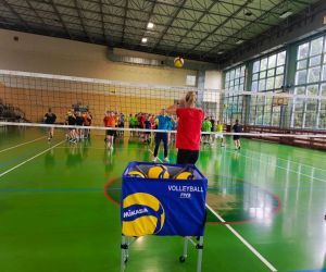 Trenerka odbija piłkę do ucznia za siatką