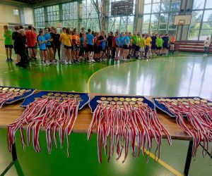 Medale leżące na stole, w tle młodzież w strojach sportowych