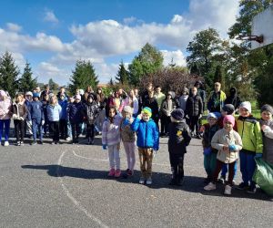 Uczniowie zgromadzeni na boisku szkolnym, trzymają w rękach worki pełne śmieci