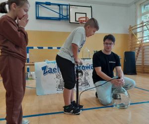 Uczeń napełnia dużą szklaną butlę powietrzem za pomocą pompki rowerowej, obok stoi uczennica