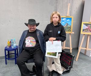 Uczennica z artystą, trzyma pracę namalowaną własnymi stopami