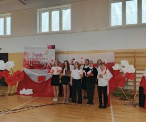 Grupa uczniów pozuje przed dekoracją „Święto Niepodległości – 11 listopada” z biało-czerwonymi kwiatami.