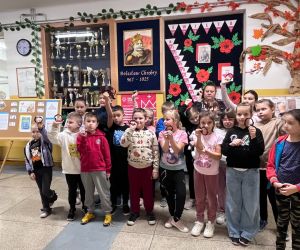 uczniowie z bransoletkami i chłopiec w koronie przy portrecie Patrona