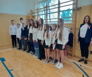 Uczniowie klasy czwartej, piątej i siódmej z nauczycielką przygotowującą uroczystość śpiewają hymn państwowy