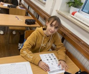 Uczennica przy stoliku rozwiązuje łamigłówkę matematyczną