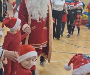 Mikołaj trzyma za rękę najmłodsze dzieci podczas wspólnej zabawy na sali gimnastycznej.