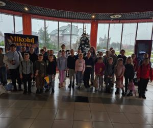 Uczniowie ustawieni w grupie w holu kina, na tle choinki i plakatu świątecznego filmu.