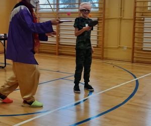 Klaun pokazuje uczniowi jak odbijać piłeczkę rakietką do tenisa stołowego.