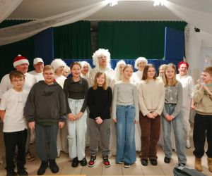 Grupa uczniów i aktorów stojąca wspólnie na tle zimowej scenografii przedstawienia „Królowa Śniegu”.