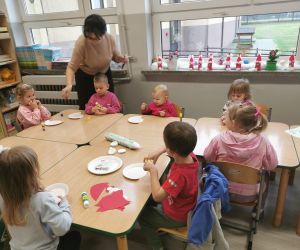 Pani pomaga dzieciom podczas zajęć plastycznych, dzieci pracują nad elementami portretu Mikołaja.