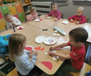 Dzieci przy stolikach wyklejają czapki i brody Mikołaja z przygotowanych materiałów.