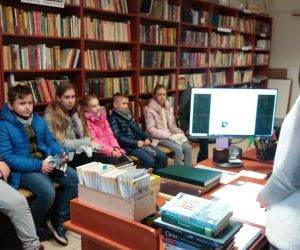 Grupa dzieci wraz z panią bibliotekarką w bibliotece.