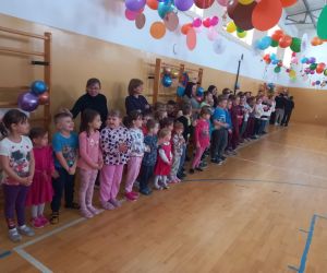 Dzieci z oddziałów przedszkolnych oraz uczniowie klas młodszych stoją w rzędzie wraz z nauczycielami.