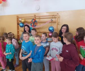 Uczniowie trzymają w rękach walentynkowe kartki, stojąc obok nauczycieli.