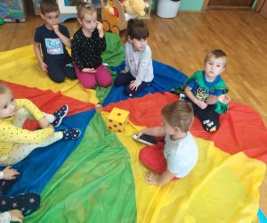 Dzieci siedzą na kolorowej chuście i patrzą na kostkę