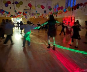 Uczniowie i nauczyciele tańczący w rytmie muzyki na udekorowanej sali gimnastycznej.