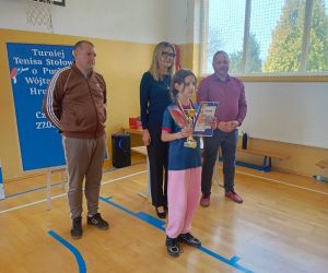 Pani Dyrektor, pan inspektor oświaty i nauczyciel wychowania fizycznego z uczennicą trzymającą puchar, dyplom i medal