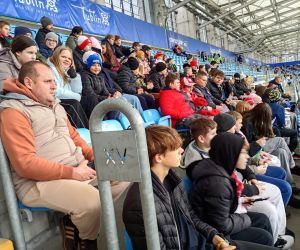 Uczniowie wraz z opiekunami siedzący na trybunach stadionu, obserwujący wydarzenia sportowe.