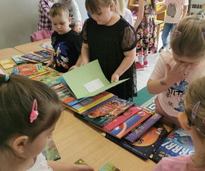Grupa dzieci przy stoliku przegląda książki, skupiając się na ilustracjach i treści.