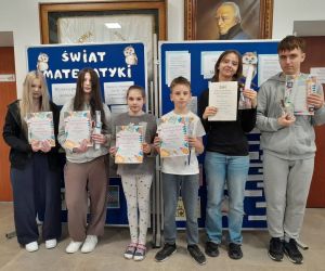 Kilku uczniów z dyplomami i upominkami stoi na tle dekoracji dotyczącej Dnia Matematyki