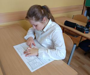 Uczennica samodzielnie pracuje nad arkuszem sprawdzianu przy szkolnej ławce.