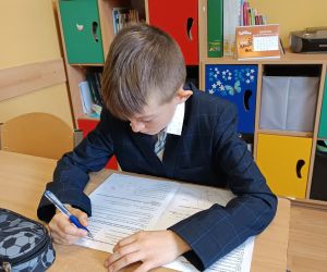 Uczeń siedzi przy ławce i rozwiązuje arkusz sprawdzianu, skupiony na zadaniach pisemnych.