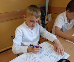 Dwóch uczniów siedzi obok siebie i w ciszy wypełnia zadania sprawdzianu.