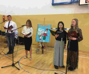 Uczniowie klasy VIII w strojach galowych śpiewają przy mikrofonach