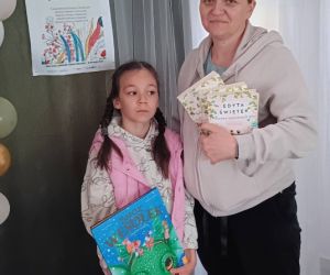 Na zdjęciu znajduje się dorosła osoba wraz dzieckiem, pozujące do zdjęcia z wypożyczonymi książkami.