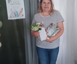 Zdjęcie przedstawia kobietę pozująca do zdjęcia z książką i notatnikiem.