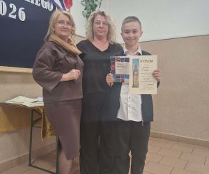 Uczeń prezentuje dyplom oraz nagrodę książkową, wykonano zdjęcie podczas uroczystego podsumowania konkursu.