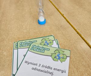 Karty edukacyjne do gry „5 sekund” o tematyce ekologicznej oraz klepsydra na stoliku.