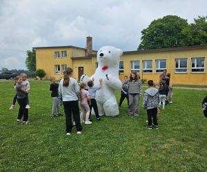 Dzieci witają maskotkę białego misia podczas wspólnej zabawy na terenie szkoły.