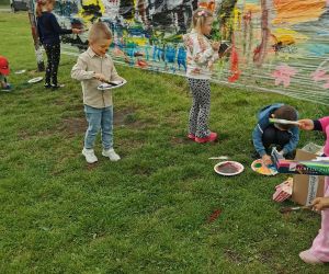 Dzieci tworzą wspólny obraz na folii rozciągniętej na bramce, malując kolorowymi farbami.