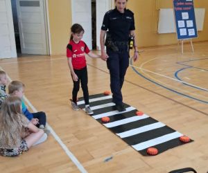 Policjantka prezentuje z uczennicą sposób właściwego przechodzenia przez przejście dla pieszych