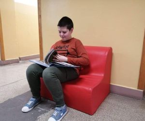 Uczeń siedzi na czerwonym fotelu i czyta na przerwie ulubioną książkę