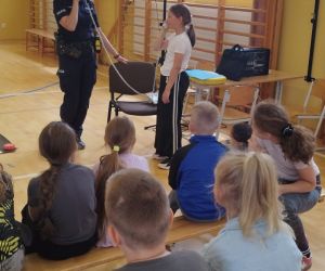 Uczennica i policjantka prezentują zebranym uczniom rozmowę z centrum powiadamiania ratunkowego