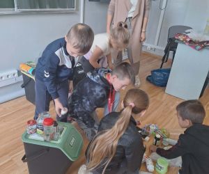  Grupa uczniów uczestniczy w zadaniu polegającym na rozpoznawaniu i segregowaniu różnych rodzajów odpadów.
