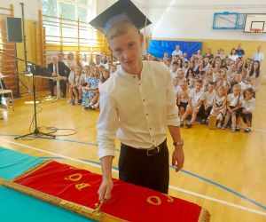 Uczeń klasy ósmej wbija pamiątkowy gwóźdź w drzewce sztandaru szkoły