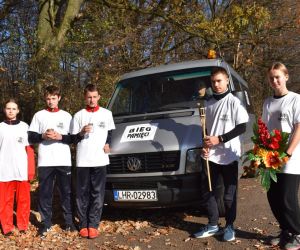 Parking. Pięć osób stoi przy samochodzie. Na samochodzie napis Bieg 
Pamięci